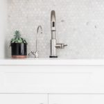 white counter top and back splash in a small kitchen with silver faucet and plant